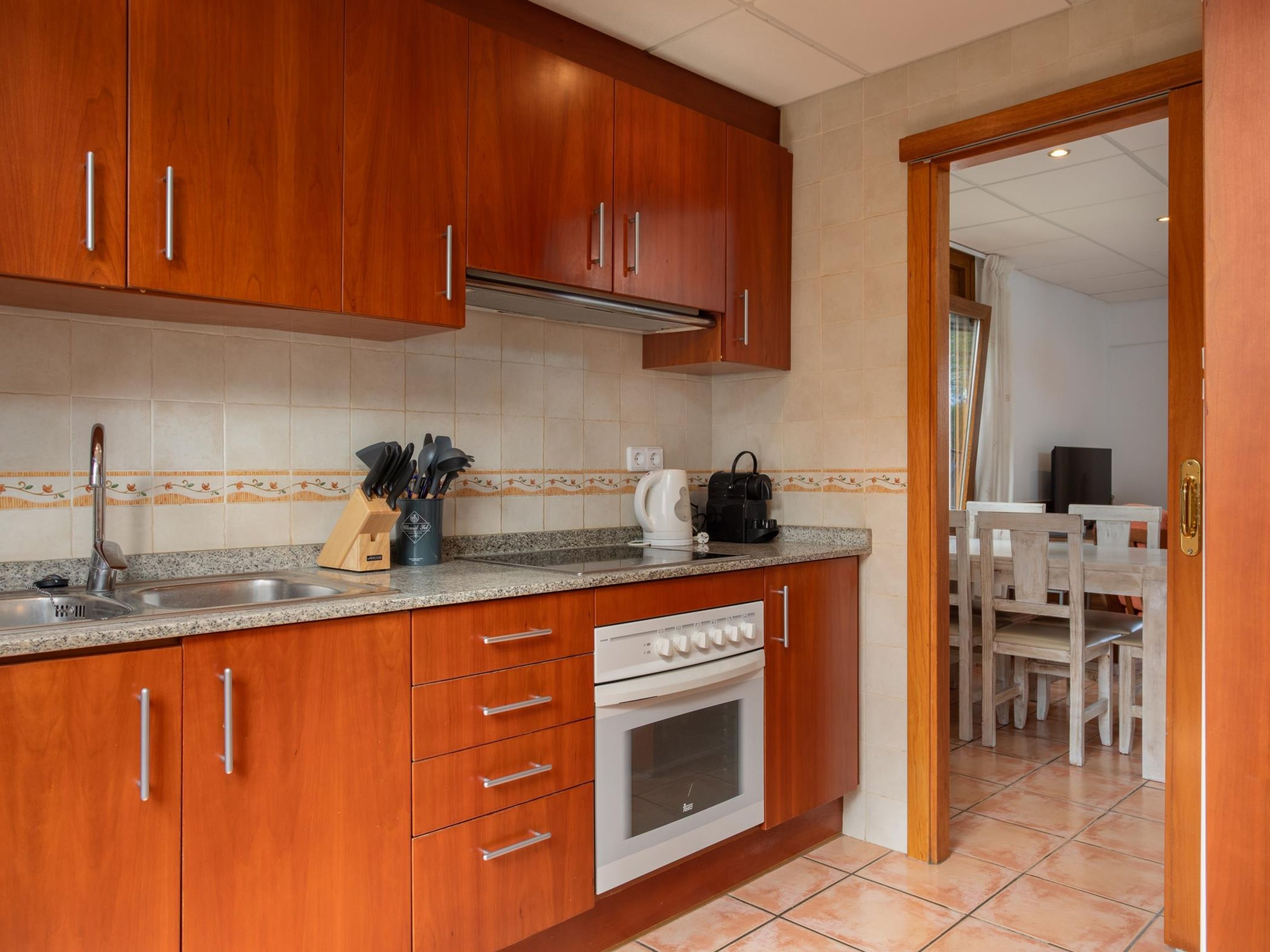Una cocina compacta con armarios de madera, un lavamanos de acero inoxidable, un horno empotrado y una cafetera.