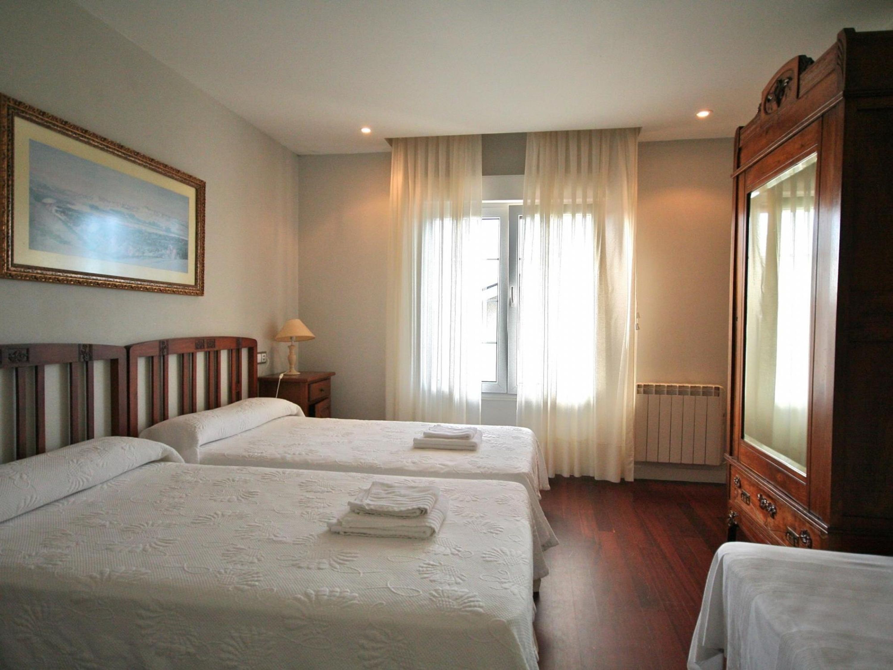 Een hotelkamer met twee bedden, een grote spiegel, een schilderij aan de muur en een raam met gordijnen.