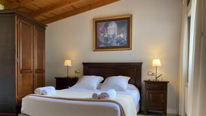 A neatly made bed with white linens and a beige throw blanket, flanked by two bedside tables with lamps, in a room with wooden flooring and a wooden ceiling.