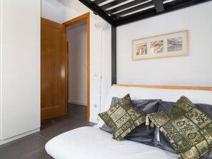 Een slaapkamer met een bed, twee kussens, een houten deur en een muur met ingelijste foto’s.