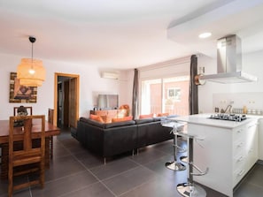 Una sala de estar moderna con un sofá negro, una mesa de comedor de madera y una cocina con encimera blanca y electrodomésticos de acero inoxidable.
