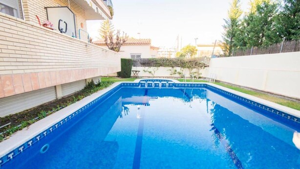 Une piscine rectangulaire à l’eau d’un bleu limpide, entourée d’un mur de briques et d’une clôture blanche.