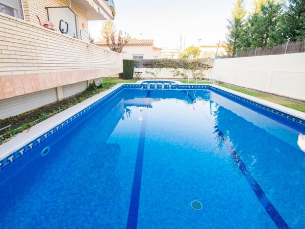 A rectangular swimming pool with clear blue water, surrounded by a brick wall and a white fence.