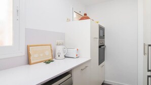 Une cuisine compacte avec des meubles blancs, un lave-vaisselle, une machine à café et un petit réfrigérateur.