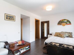 Un dormitorio moderno con una cama grande, una mesita de noche de madera, un sillón de lectura y una pequeña mesa con libros y objetos decorativos.