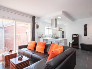 A modern living room with a leather sofa, orange cushions, a coffee table, and a kitchen in the background.