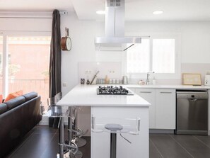 A modern kitchen with a central island, stainless steel appliances, and a dining area with a black leather sofa. - Sunny Apartment 3 Blocks to the Beach (Castelldefels)
