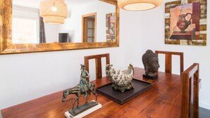 Un coin repas comprenant une table en bois, des chaises, un grand miroir et des objets décoratifs, notamment une statue, un coq en céramique et un vase.