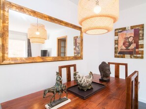 Een eetgedeelte met een houten tafel, stoelen, een grote spiegel en decoratieve items, waaronder een beeldje, een keramieken haan en een vaas.