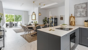A modern kitchen with a central island, dark cabinetry, and a dining area with a large window.