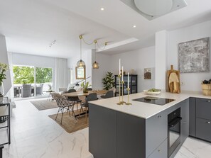 A modern kitchen with a central island, dark cabinetry, and a dining area with a large window.