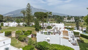 A residential area with white houses, green lawns, and a mountain in the background.