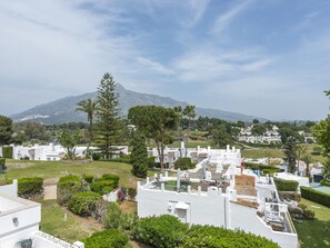 A residential area with white houses, green lawns, and a mountain in the background.