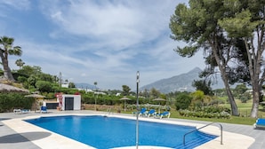 A swimming pool with blue water, surrounded by a tiled deck, and a mountain view in the background.