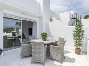 A patio with wicker furniture, a potted plant, and a view of the surrounding area.