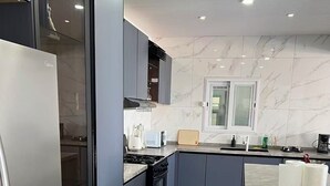 Una cocina moderna con armarios grises, un refrigerador de acero inoxidable, una estufa a gas y una ventana con persianas.