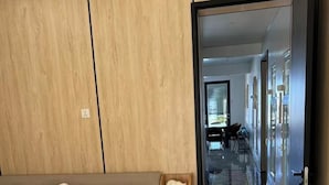 Un dormitorio moderno con cabecera de madera, cama con ropa de cama blanca, una mesita de noche de madera con una figurita de gato y un pasillo que conduce a un comedor.