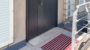 Entrada de un edificio moderno con una puerta negra grande, una escalera metálica y una alfombra roja que sube.