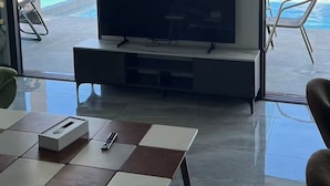 Una sala de estar moderna con un televisor de pantalla plana sobre un mueble bajo pared, una mesa de centro y vistas a una piscina y barcos.