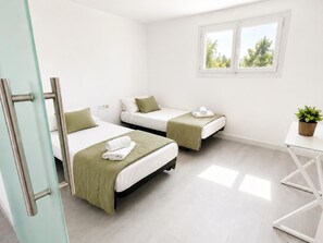 A hotel room with two beds, a small table, a window, and a door.