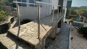 A modern house with a stone terrace, a metal railing, and a view of the countryside. - Villa Independiente con Piscina y Vistas (Sant Pere de Ribes)