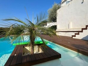 Una piscina con muelle de madera, una palmera y un edificio blanco con el número 7.