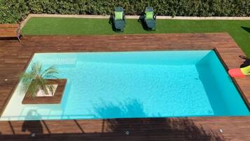 A rectangular swimming pool with a wooden deck, a palm tree, and two green lawnmowers.