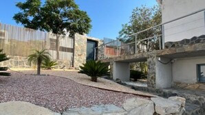 A courtyard with a stone wall, a palm tree, and a building with a stone facade. - Villa Independiente con Piscina y Vistas (Sant Pere de Ribes)