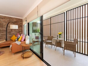 A modern living room with a brick wall, a glass door leading to a balcony, and wicker furniture.