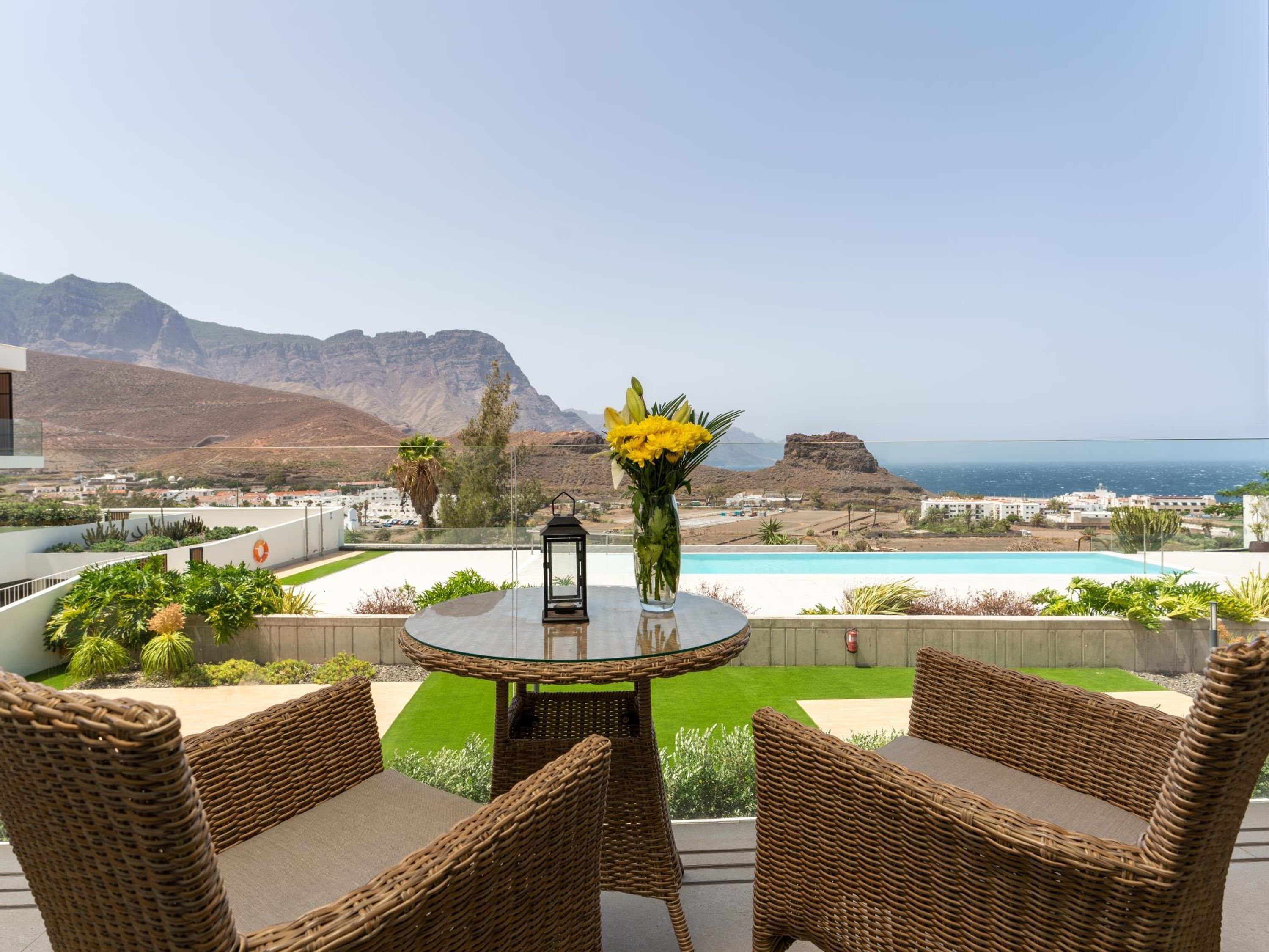 A terrace with wicker furniture, a glass table, and a vase of yellow flowers.