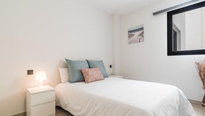 Une chambre à coucher au style minimaliste, avec un lit, des tables de chevet, une lampe et un miroir fixé au mur.