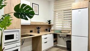 Una cocina moderna con horno, microondas y refrigerador integrados. Tiene una encimera de madera, un lavamanos y una ventana con persianas.