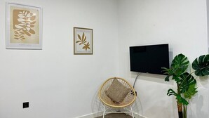 Una habitación con una televisión montada en la pared, una silla de mimbre y dos láminas botánicas enmarcadas.
