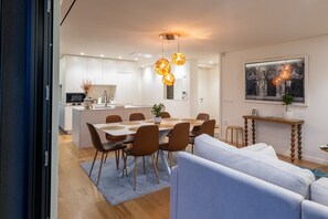 A modern kitchen with a dining area, featuring a central island, pendant lighting, and a large window with a view.