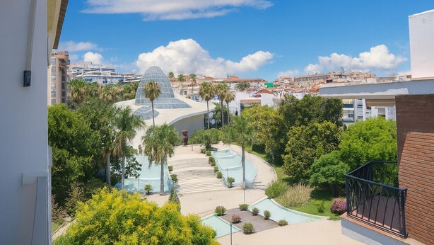 A view of a swimming pool area with a modern architectural building in the background. - Apartamento Orquidario (Estepona)