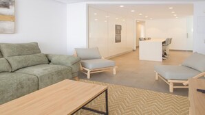 A modern living room with a sofa, two armchairs, a coffee table, and a kitchen area in the background. - Apartamento Orquidario (Estepona)