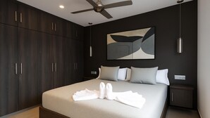 A modern bedroom with a large bed, dark wood wardrobe, and a ceiling fan. - Apartamento Orquidario (Estepona)