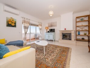 Ein Wohnzimmer mit einer Couch, einem kleinen Tisch, einem Kamin und einem Balkon mit Vorhängen.