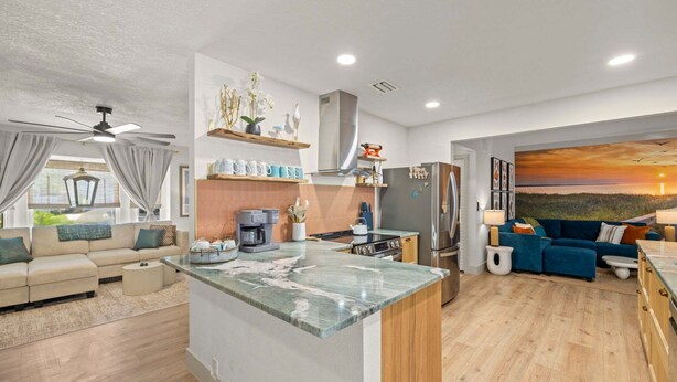 Una cucina moderna con isola centrale, una zona pranzo con divano blu e un soggiorno con divano beige.