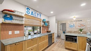 Una cucina moderna con mobili in legno, un forno a microonde integrato e un piano di lavoro con bicchieri e oggetti decorativi.