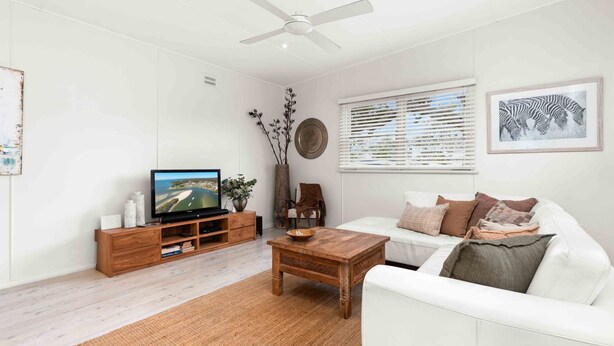 Una sala de estar moderna con televisor de pantalla plana, mueble de entretenimiento de madera, sofá blanco y una mesa de centro.