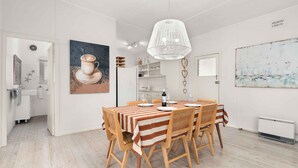 Un comedor con una mesa preparada para dos personas, sillas de madera, una lámpara colgante blanca y un cuadro de una taza en la pared.