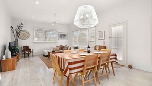 Amplia sala de estar con comedor, que presenta una gran mesa con manteles a rayas, sillas de madera y una lámpara colgante.