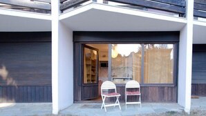 A modern house with a covered patio, two white chairs, and a sliding glass door leading to a garage. - 50m from ski slopes, Ground floor, view mountain, parking, tv, ski locker, 18m², Montgenèvre (Montgenèvre)