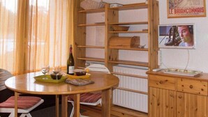 A cozy room with a wooden dining table set for two, a radiator, and a shelf unit with a poster. - 50m from ski slopes, Ground floor, view mountain, parking, tv, ski locker, 18m², Montgenèvre (Montgenèvre)
