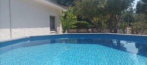 Piscina com azulejos azuis, cercada por um edifício branco e árvores.
