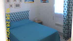 A bedroom with a bed, a nightstand, a window with curtains, and wall art. - 50 m from the beach (Agde)