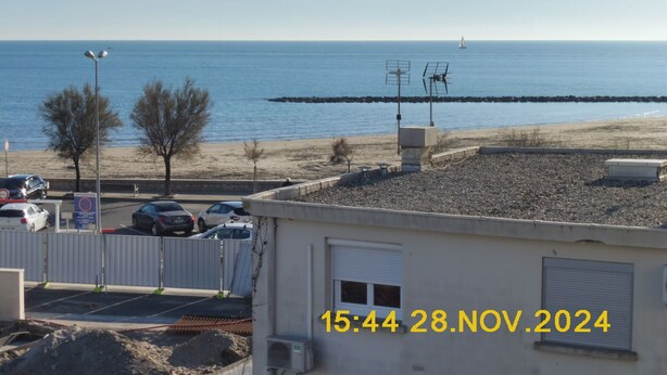 A coastal view with a beach, parked cars, and a building with a closed shutter. - 50 m from the beach (Agde)
