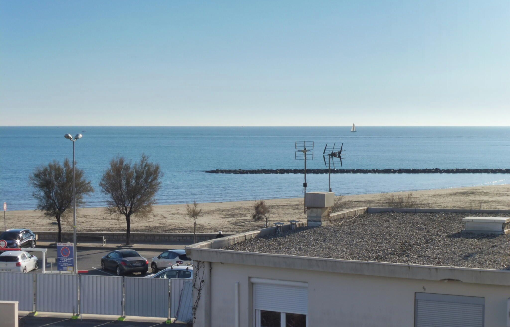 Blick auf die Küste mit Strand, geparkten Autos und einem Gebäude mit heruntergelassenen Rollläden.