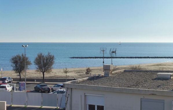 A coastal view with a clear sky, a sandy beach, and a rocky breakwater.